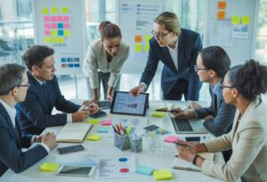 A group of business professionals collaborating around a table with marketing materials and digital devices in a bright office.
